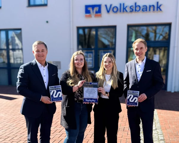 Vier Personen (von links nach rechts Matthias Kruse, Laura-Sophie Sukkau, Larissa Lorenz und Matthias Smit)  stehen im Außenbereich vor einem Volksbank-Gebäude mit sichtbarem Logo über dem Eingang. Die Gruppe hält jeweils „kununu Top Company 2025“-Auszeichnungen in den Händen. Im Hintergrund sind die Fassade des Gebäudes, Fenster und der gepflasterte Vorplatz bei Tageslicht zu sehen.